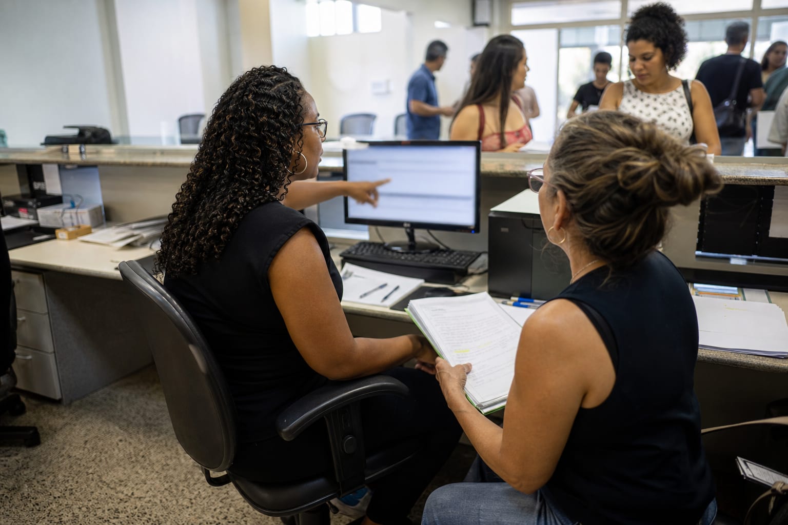 Funcionárias de secretaria comparando dados entre computador e pasta de papéis